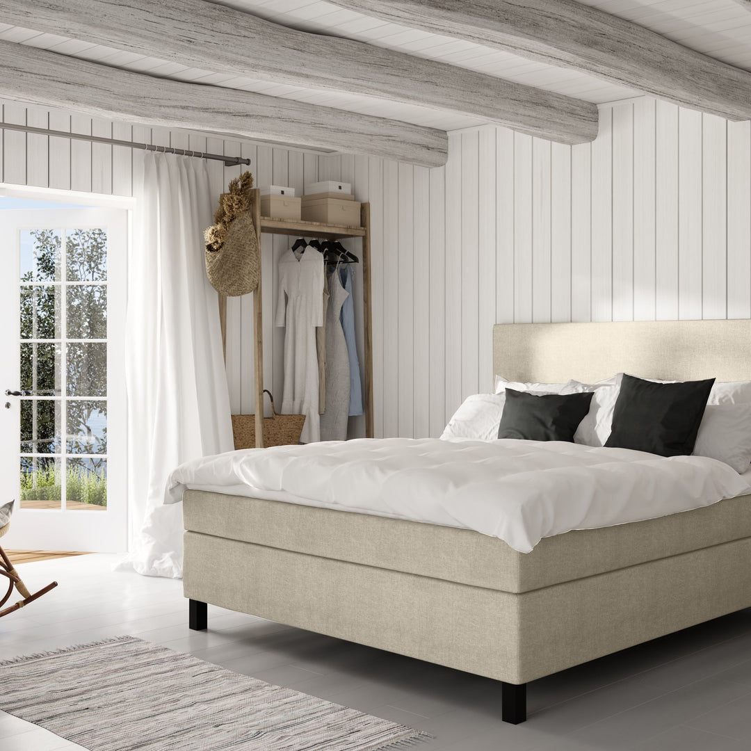 Wonderland W50 sengegavl i beige, oppredd seng i lyst panelt soverom med klesstativ og teppe