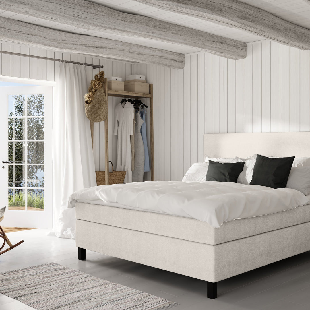 Wonderland W50 sengegavl i kremhvit, oppredd seng i lyst panelt soverom med klesstativ og teppe