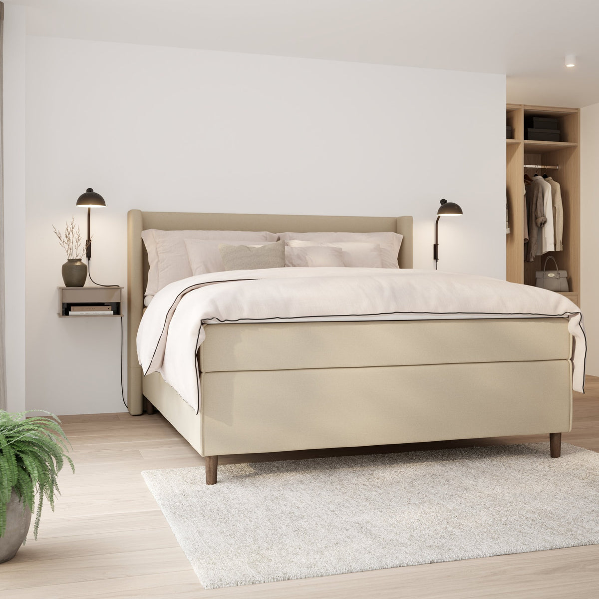 Wonderland Wing sengegavl i lys beige stoff, oppredd seng med vegglamper, nattbord og grønn plante i soverom.