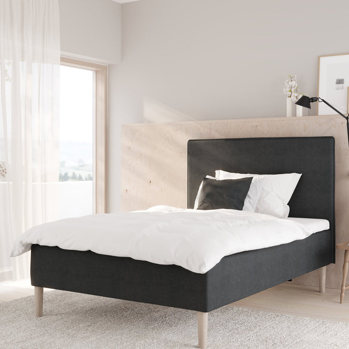 Wonderland Lento rammeseng i lys sandbeige stoff med hvit dyne, mot hvit panelvegg med åpen garderobe.
