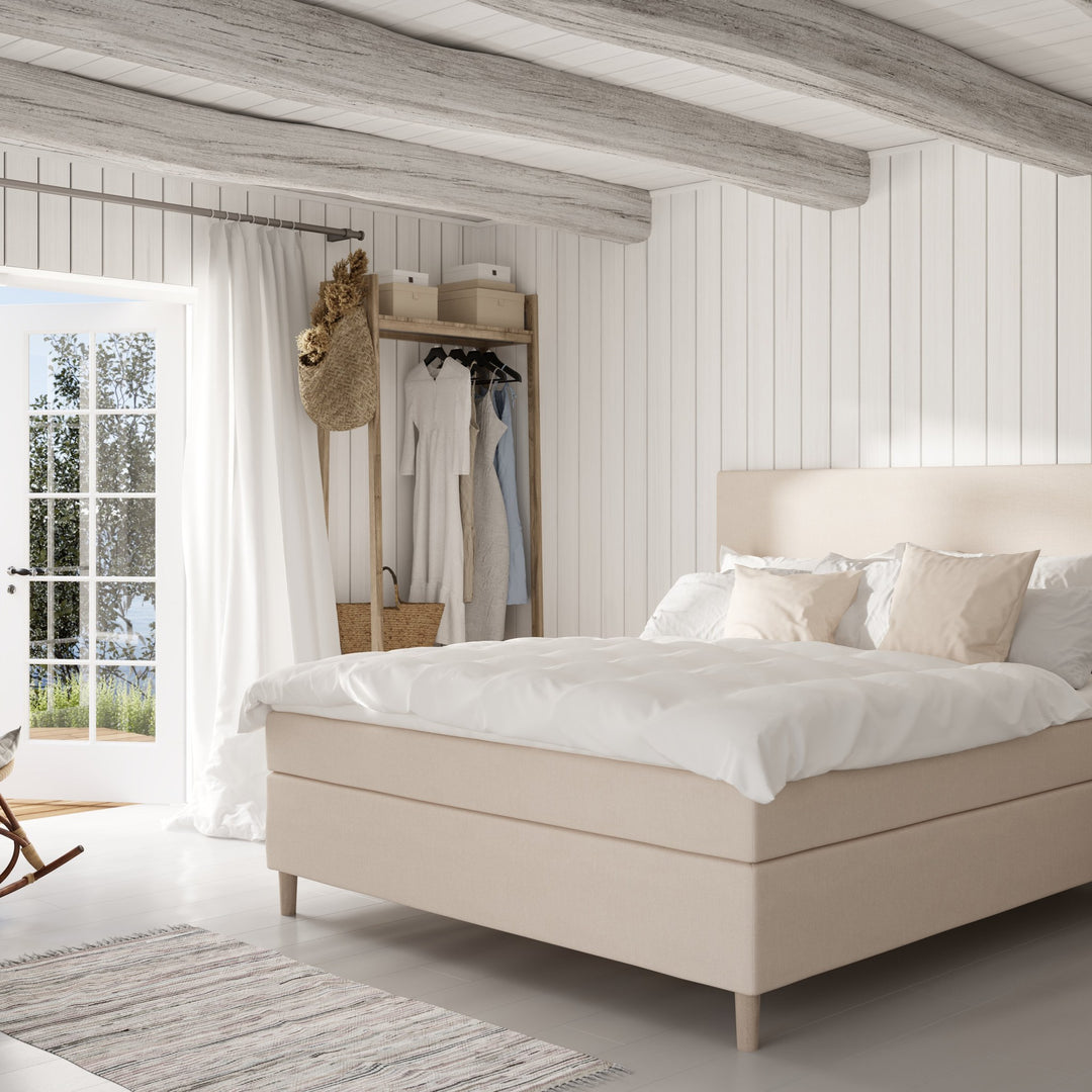 Wonderland Lento kontinentalseng i beige i lyst hytterom med hvit panel og klesstativ