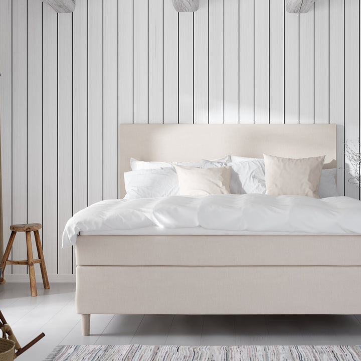 Wonderland Lento kontinentalseng i lys beige, oppredd mot hvit panelvegg med krakk og fillerye