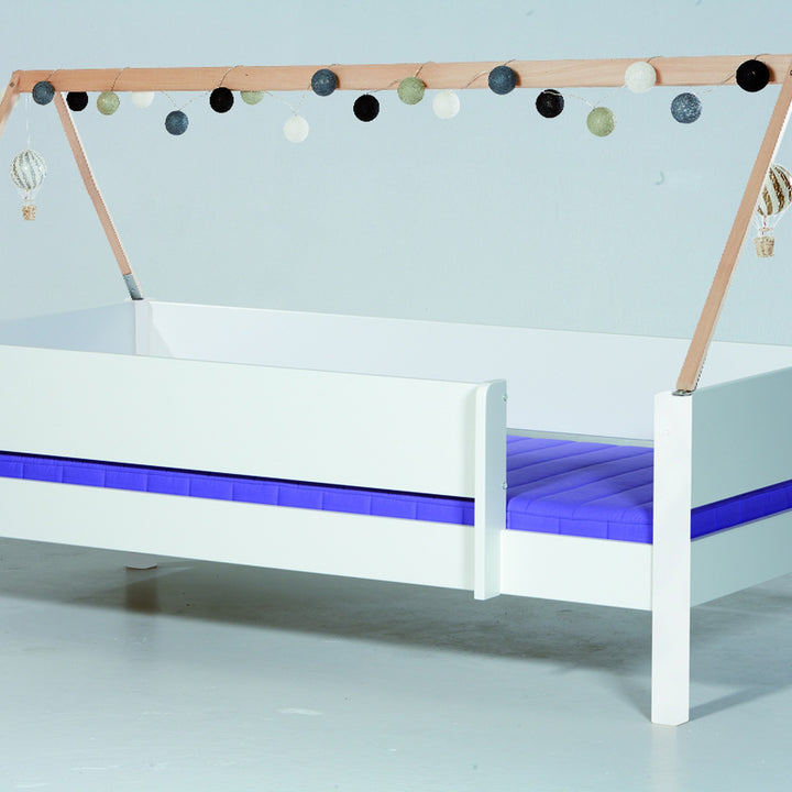 Manis-h trestativ i tre over hvit barneseng, pyntet med kulelysslynge og luftballonger